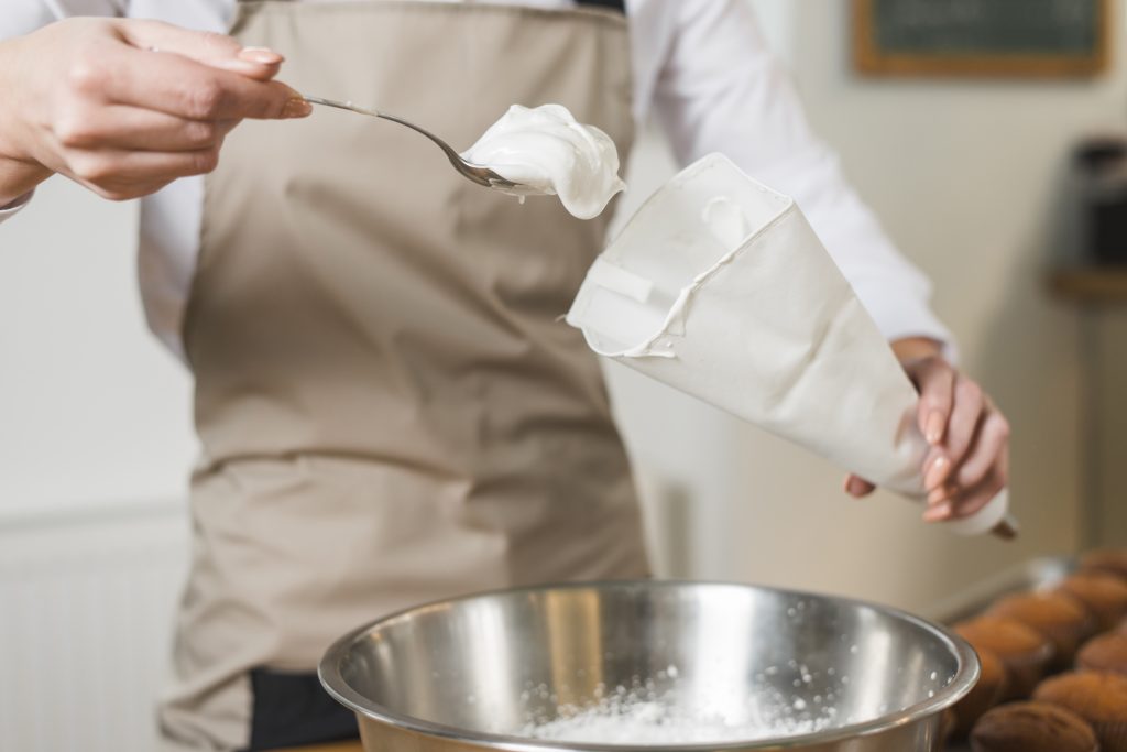 Padeiro feminino enchendo creme chantilly no saco de confeiteiro branco